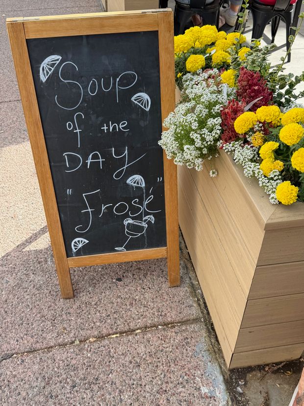 A sidewalk chalkboard advertising frose beside bright flowers